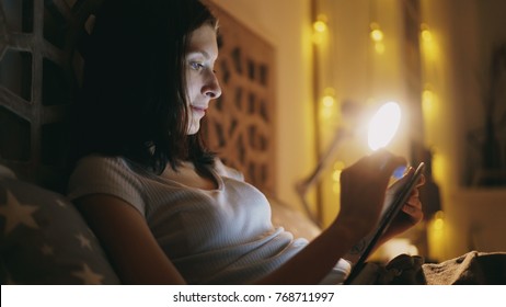 Happy Smiling Woman Using Tablet Computer For Sharing Social Media Lying In Bed At Home At Night