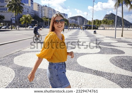 Happy smiling woman walking along Copacabana beach promenade and turns to the camera, Rio de Janeiro, Brazil
