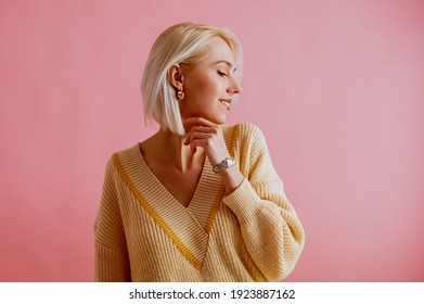 Happy smiling woman wearing trendy yellow v-neck sweater, elegant silver wrist watch, golden earrings, posing on pink background. Spring fashion conception. Copy, empty space for text
