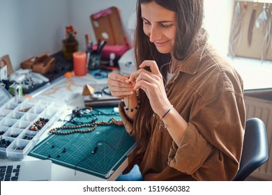 Happy smiling woman is working on beads jewellery at her own workplace.