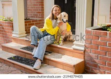 happy smiling woman in yellow sweater walking at her house with a dog golden retriever breed, having fun together, summer style casual outfit