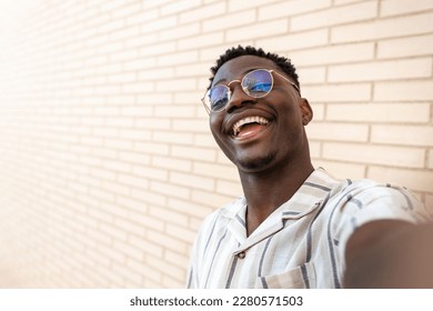 Happy, smiling young African American man with glasses taking selfie. Copy space. Brick wall background. - Powered by Shutterstock