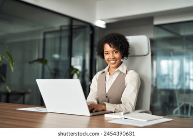 Happy smiling young African American professional business woman manager executive or female lawyer entrepreneur looking at camera at workplace working on laptop computer in office, portrait. - Powered by Shutterstock