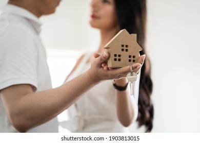 Happy smiling young asian couple holding a model house, and danceing together with feeling happiness when they have new house. Young loving couple with small wooden house new home concept