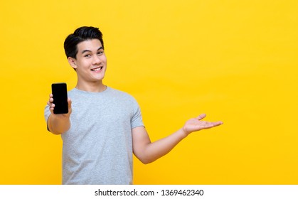 Happy Smiling Young Asian Man Showing Mobile Phone With Another Hand Open On Colorful Yellow Background