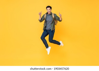 Happy smiling young Asian tourist man with backpack jumping and giving thumbs up isolated on yellow background - Shutterstock ID 1903457620