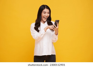 Happy smiling young asian woman using mobile phone isolated on yellow background. teen social media communication online.