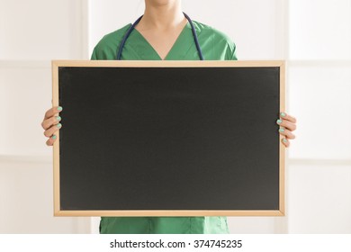 Happy smiling young beautiful female doctor showing blank area for sign or copy space. Nurse showing blank clipboard sign - medical concept. Closeup on doctor woman holding blackboard