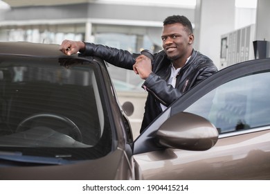 Happy Smiling Young Black Man, Holding Take Away Coffee Cup, And Leaning On His Car, While Posing To Camera At Petrol Station