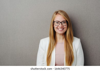 Happy lächelnde junge blonde Frau mit Brille und einer stylischen weißen Jacke auf grauem Studiohintergrund mit Kopienraum