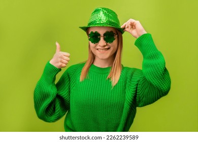 Happy smiling young blonde woman in green knitted sweater with clover shaped glasses holding green party hat and showing thumb up or holding finger up isolated on green background.

St Patricks day. - Powered by Shutterstock