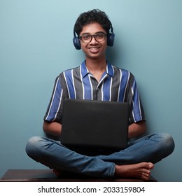 Happy smiling young boy of Indian ethnicity wearing headset and holding a laptop