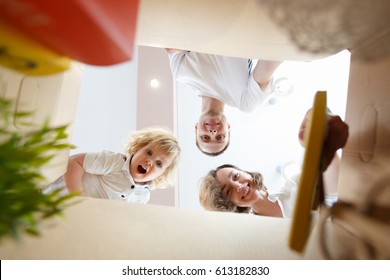 Happy Smiling Young Family With Little Baby Boy Opening An Unpacked Carton Box And Looking Inside, Relocation And Moving Concept. Mom, Dad And Kid Unpack Boxes