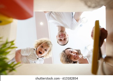 Happy Smiling Young Family With Little Baby Boy Opening An Unpacked Carton Box And Looking Inside, Relocation And Moving Concept. Mom, Dad And Kid Unpack Boxes