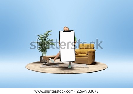 Happy smiling young girl holding giant 3D model of mobile phone with empty screen for text, ad over blue background with home interior. Online shopping, freelance. Mockup for design, logo.