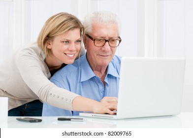 Happy smiling young girl teaching and showing new computer technology to her grandfather - Powered by Shutterstock