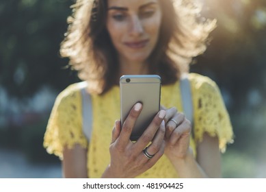 Happy Smiling Young Girl Using Modern Smartphone Outside, Beautiful Woman Typing Text Message Or An Sms Via Her Cellphone While Walking In The Park At Sunny Summer Day, Flare Light