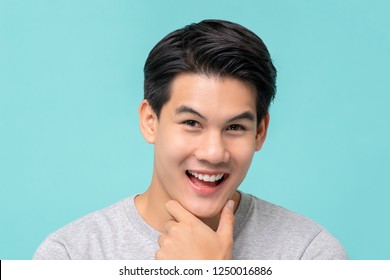 Happy Smiling Young Handsome Asian Man Face With Hand Touching Chin Studio Shot Isolated On Light Blue Background