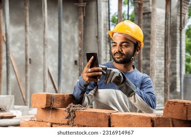 Happy smiling young indian construction labour busy on mobile phone at workplace - Powered by Shutterstock