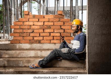 Happy smiling young indian construction labour busy on mobile phone at workplace - Powered by Shutterstock