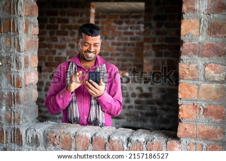 Happy smiling young indian labour busy on mobile phone at workplace - concept of using social media application, technology and leisure activity.