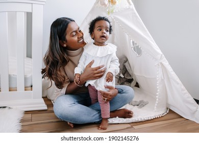 Happy Smiling Young Indian Mother Playing With Black Baby Girl Daughter. Family Mixed Race People Mom And Kid Together Hugging At Home. Authentic Candid Lifestyle With Infant Kid Child. 