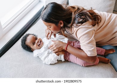 Happy Smiling Young Indian Mother Playing With Black Baby Girl Daughter. Family Mixed Race People Mom And Kid Together Hugging At Home. Authentic Candid Lifestyle With Infant Kid Child. 