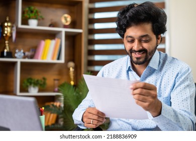 Happy Smiling Young Man Reading Offer Or Promotional Letter While Sitting At Office - Concept Of Achievement, Loan Approval And Job Promotion