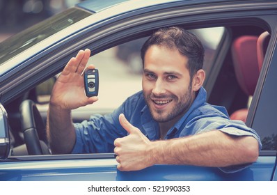 Happy, Smiling, Young Man Sitting In His New Blue Car Showing Keys Thumbs Up Isolated Outside Dealership Lot. Personal Transportation Purchase Concept