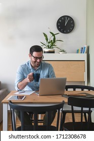 Happy Smiling Young Man Watching And Working On Computer Laptop At Home And Drinking Coffee Or Tea Stock Photo