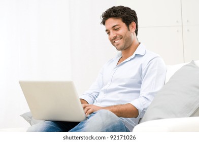 Happy smiling young man watching and working on computer laptop at home