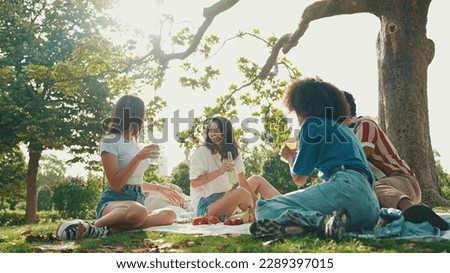 Happy smiling young multinational people at picnic on summer day outdoors. Friends have fun weekend together, relaxing in the park at picnic