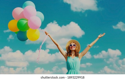 Happy Smiling Young Woman With Bunch Of Colorful Balloons Wearing A Summer Straw Hat On The Field On A Blue Sky Background