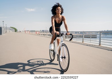Happy smiling young woman curly-haired contented activity road bike riding in a sports black suit. - Shutterstock ID 2252559227