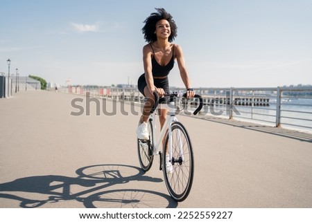 Happy smiling young woman curly-haired contented activity road bike riding in a sports black suit.