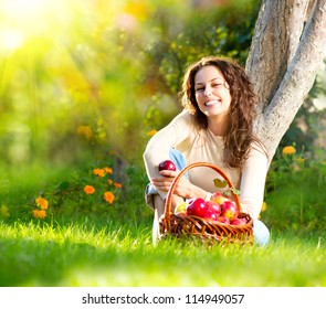 Happy Smiling Young Woman Eating Organic Apple in the Orchard.Basket of Apples. Harvest Concept.Garden - Powered by Shutterstock