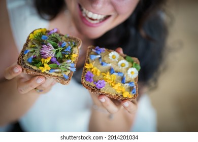 Happy Smiling Young Woman Eating Vegan Cream Cheese Substitute Whole Grain Bread Slicce Or Toast Flowery Decorated With Daisy, Dandelion And Meadow Flowers For A Healthy Breakfast Or Snack