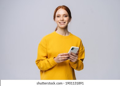 Happy Smiling Young Woman Holding Mobile Phone And Looking At Camera On Isolated White Background. Pretty Redhead Lady Model Emotionally Showing Facial Expressions In Studio, Copy Space.