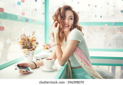 Happy Smiling Young Woman Using Phone In A Cafe. Beautiful Girl In Trendy Spring Colors. 