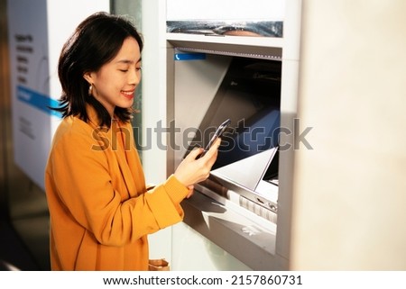 Happy smiling young woman withdrawing money from credit card. Young woman typing pin code on keypad of ATM machine	