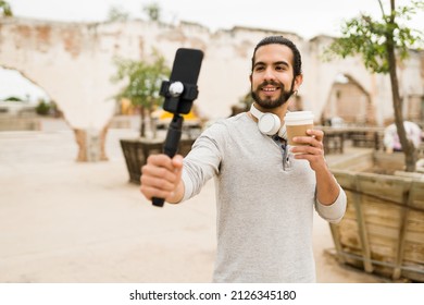 Happy social media influencer filming himself with a smartphone and recording a story or online reel while drinking coffee