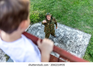 Happy Soldier Reunited With His Son After Coming Back From War. Excited Boy Standing On Terrace With Open Arms For Hug, Looking At Military Dad In Camouflage. Veteran Of War Or Returning Home Concept.