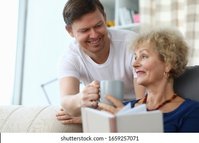 Happy Son Brought Cup Tea For An Elderly Mother. Son Cares For An Elderly Mother At Home. An Adult Son Decided To Stay With His Mother Alone. Have Fun With Your Parents. Good Family Relationships