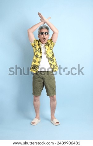 HAPPY SONGKRAN DAY. Asian tourist senior man in summer clothing with gesture of  stop, forbid, refusing isolated on blue background. Songkran festival. Thai New Year's Day.