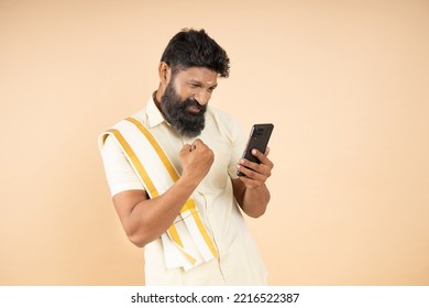 Happy South indian man with winning expression using mobile phone isolated on beige background, He is wearing traditional white dress. jackpot or lottery - Shutterstock ID 2216522387