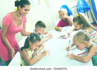 Happy Spanish  Children Making Writing Exercises With Help Of Teacher In Class 