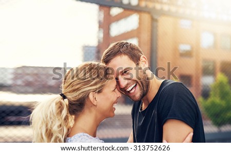 Happy spontaneous attractive young couple share a good joke laughing uproariously and hugging each other outdoors in an urban environment