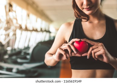 Happy sport woman holding red heart in fitness gym club. Medical cadio heart strength training lifestyle. Pretty female sport girl workout exercise. Cardiac healthy and wellbeing. Massage ball in hand - Shutterstock ID 1165619149