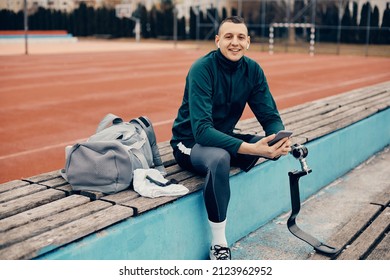 Happy sportsman with artificial leg cell phone and listening music over earbuds while relaxing at outdoor sports field and looking at camera. - Powered by Shutterstock