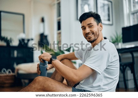 Happy sportsman drinking water while exercising at home and looking at camera.  